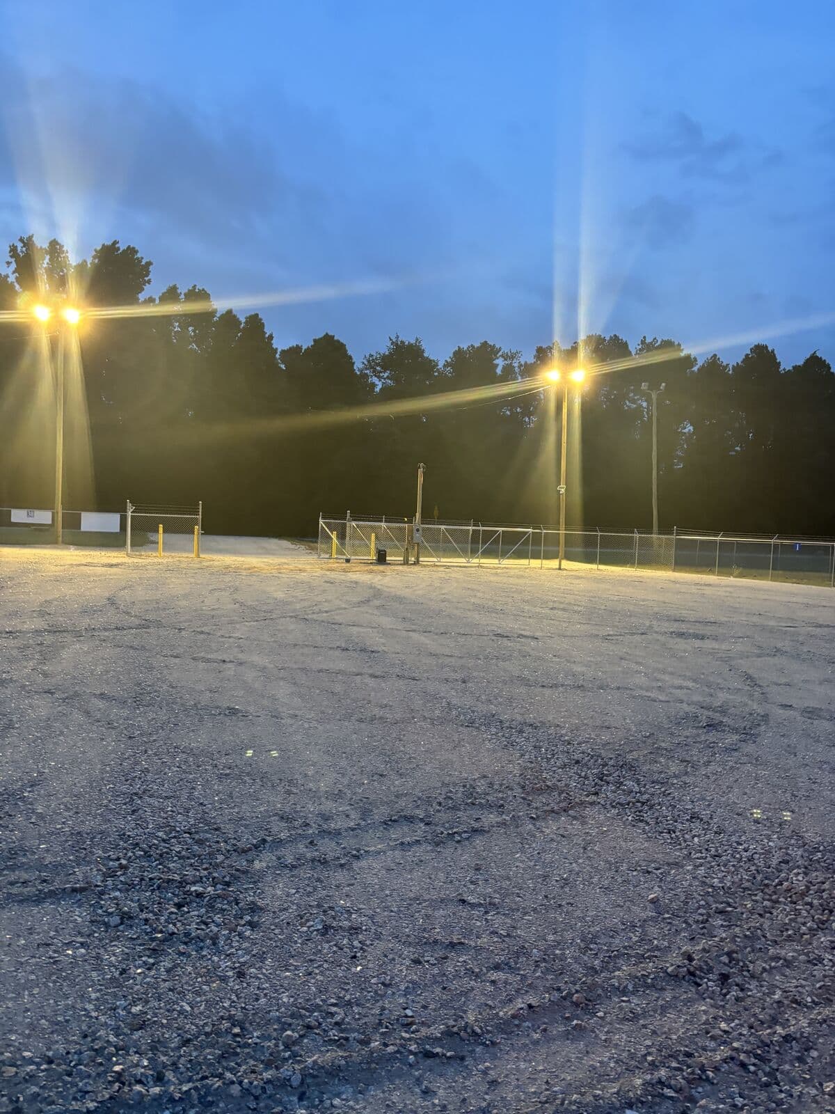 Bright pole lighting illuminating the gravel lot at dusk